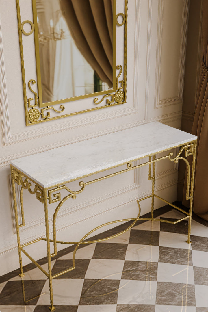 Gold console table with marble top in a room with a mirror and curtains.