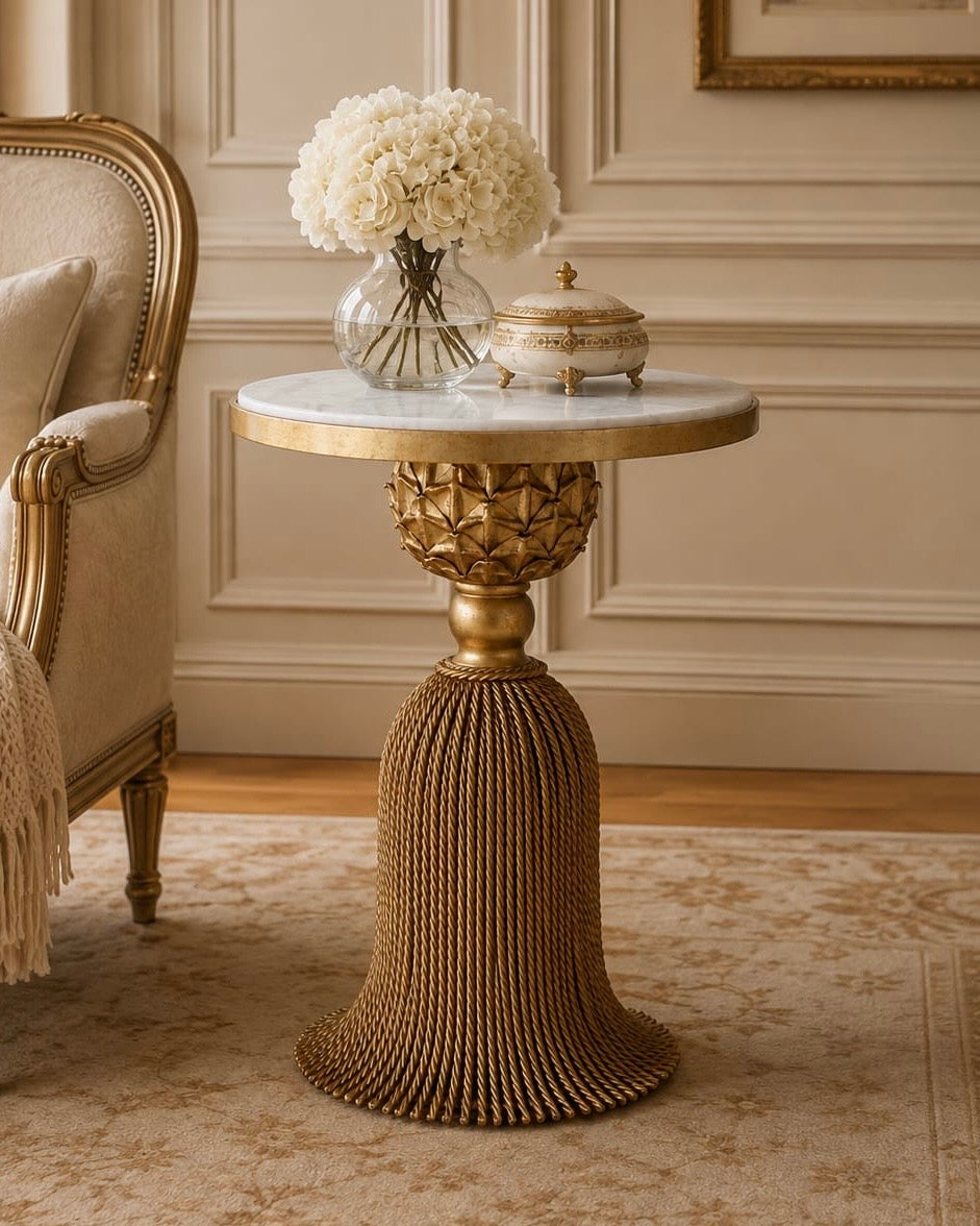 Isadora gold wrought iron side table with sculptural tassel base, white marble top, and floral detailing in an elegant classic interior.