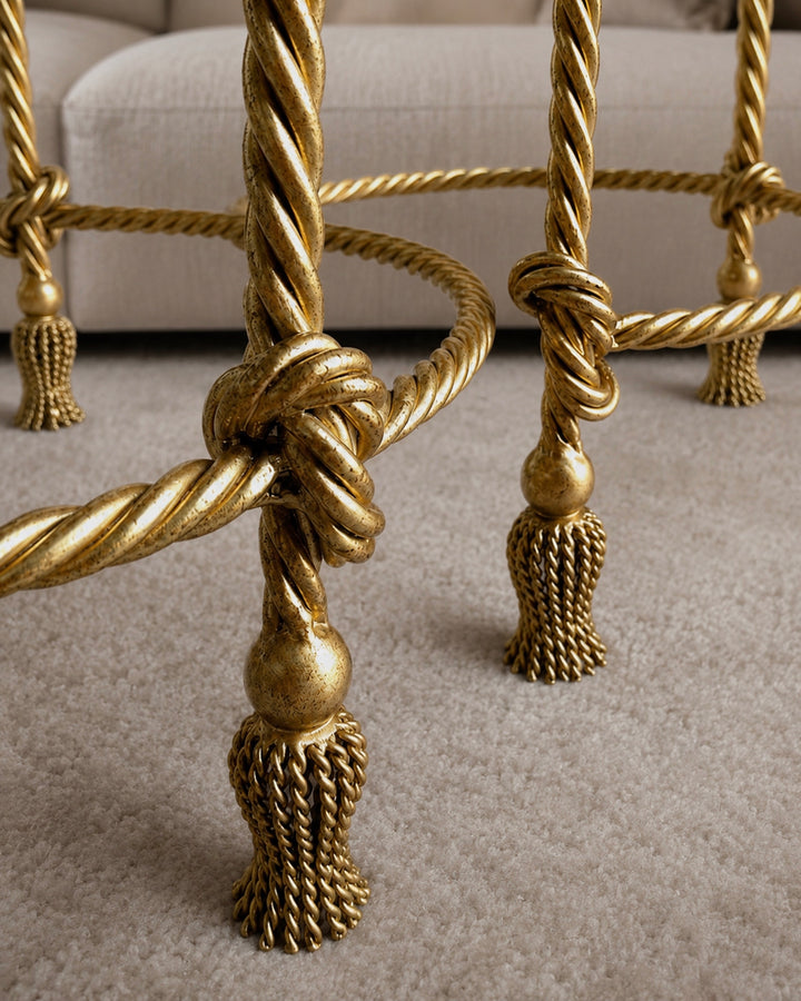 Close-up of Allegra nesting table legs with gold rope-knot detailing and tassel feet on a soft carpet.