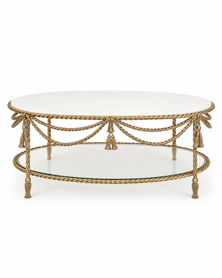 An oval coffee table featuring a white marble top, a gold rope-finish metal frame with decorative tassels, and a lower glass shelf, shown against a plain white background.