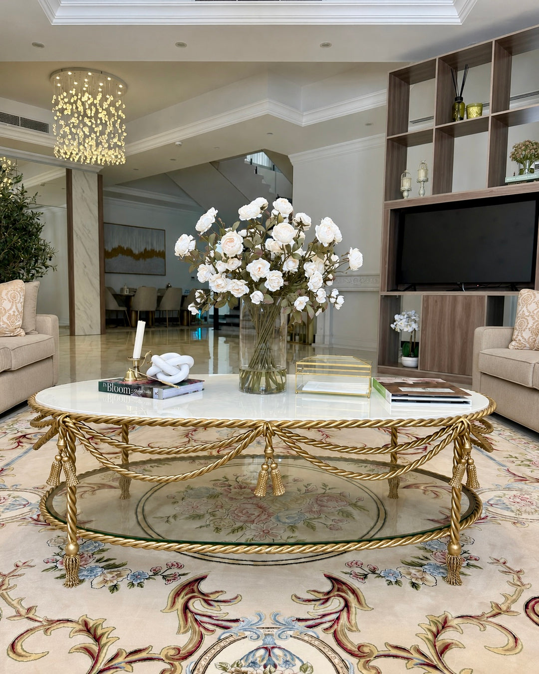 Allegra Oval Center Table featuring a handcrafted antique gold wrought iron frame with twisted rope detailing, white marble top, and tempered glass lower shelf in a luxury living room.