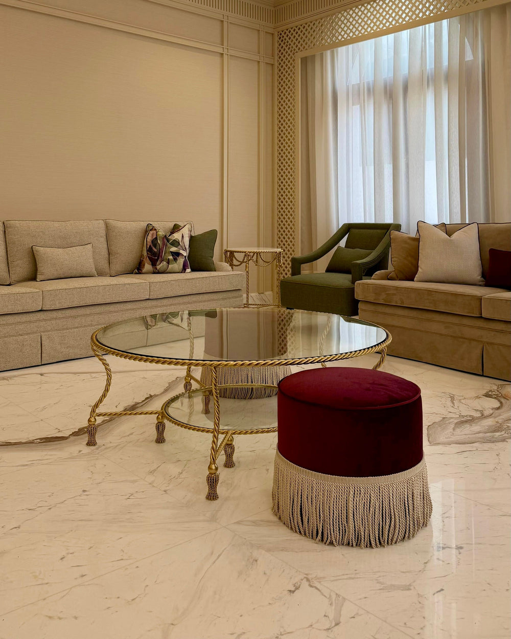 Allegra Round Center Table in gold-finished wrought iron with twisted rope detailing, tassel feet, and two clear glass tiers in an elegant living room.