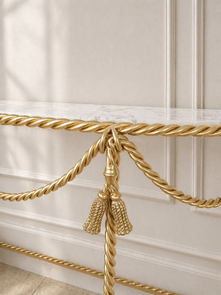 Console close up of gold decorative rope with tassel against a beige wall.