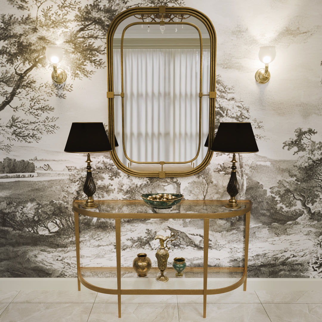 Selina half-moon console with a brushed gold frame, styled with a tall tiered mirror and black-shaded lamps, set against a classical mural background.