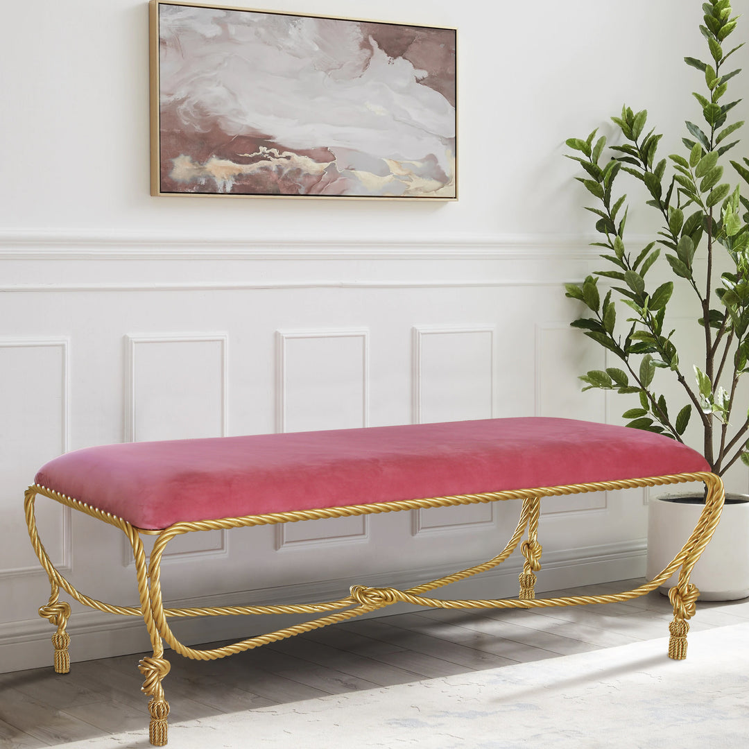 A rope-themed metal golden bench topped with pink velvet upholstery in a luxurious living space