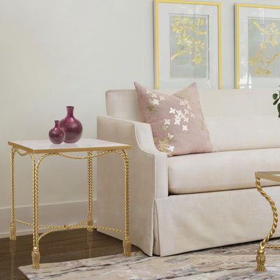 Twisted metal rope-themed side table in golden color and marble top stands at the end of a pink sofa