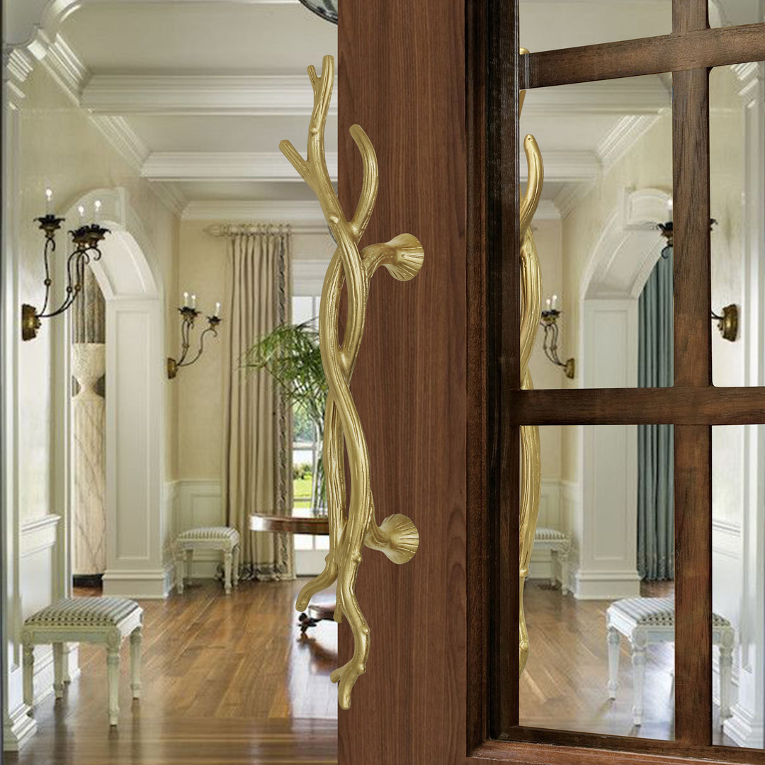 A pair of golden accent pull handles inspired by twisted branches mounted on an opened wooden door with glass inlay
