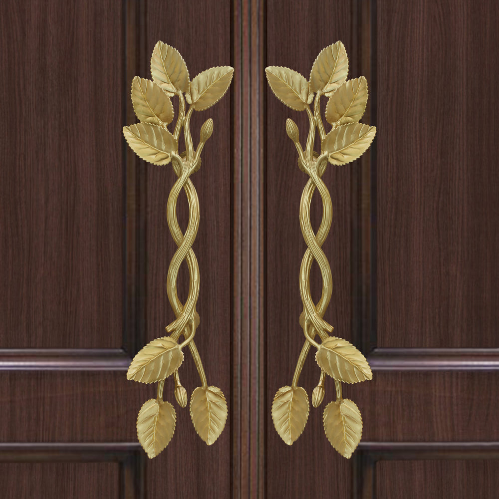 A pair of golden decorative pull handles inspired by branches, leaves and buds mounted on a closed wooden door