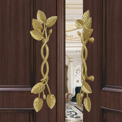 A pair of golden decorative pull handles inspired by branches, leaves and buds mounted on an opened wooden door