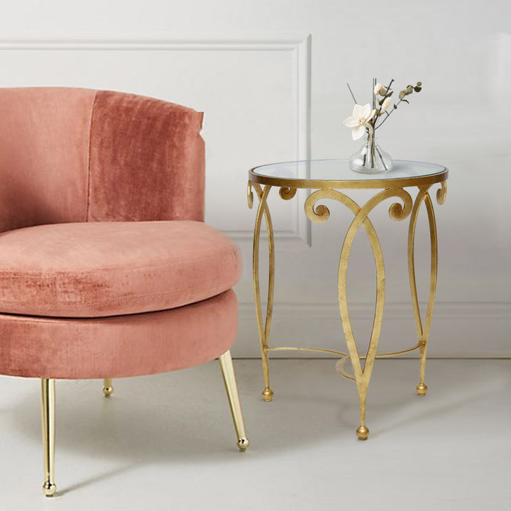 An exquisite golden end table made up of metal scrolls stands beside a pink arm chair