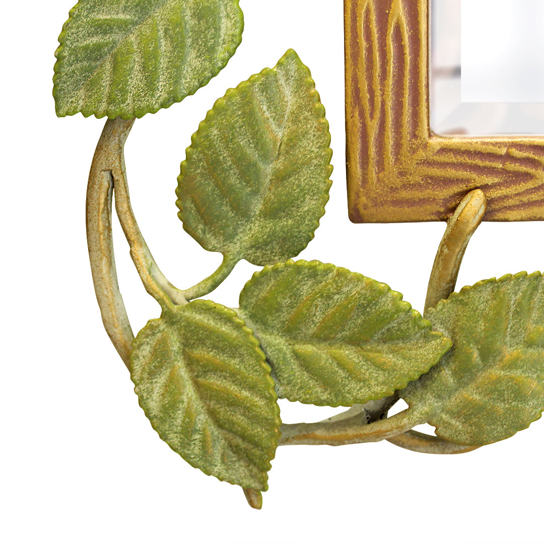 Close up of a mirror inspired by nature with metal leaves and branches along its border, painted in natural colors