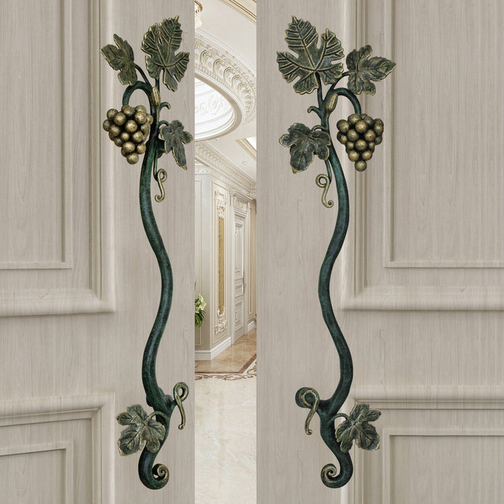 A pair of dark green and gold luxurious pull handles inspired by grape vines mounted on an open wooden beige door