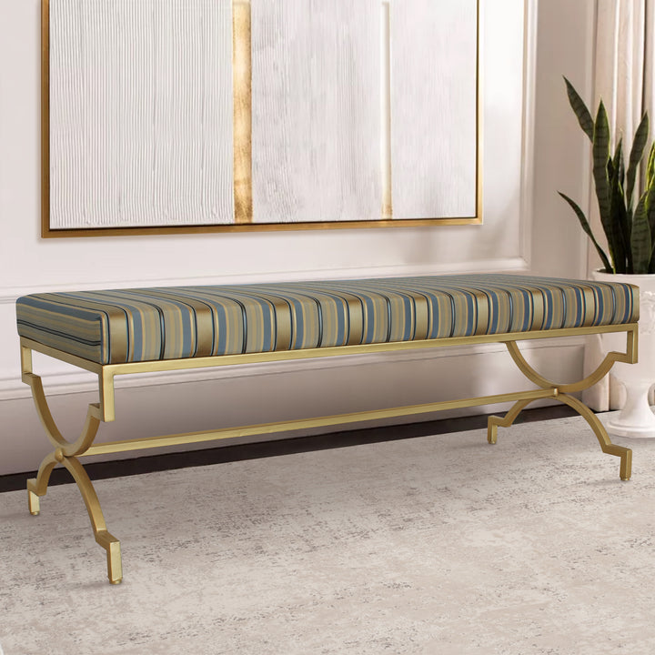 A contemporary metal golden bench topped with stripy blue silk upholstery in a living space