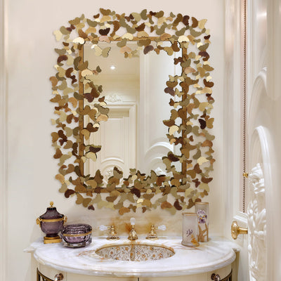 A unique metal rectangular mirror with butterflies along its border painted in a golden finish; hangs above a washroom sink