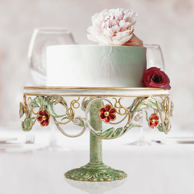 A cake sits on a decorative floral stand on a table