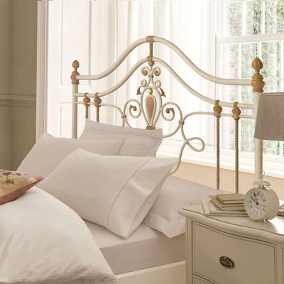 A girly wrought iron single bed with scrolls, leaves and motifs painted in white, pink and hints of gold