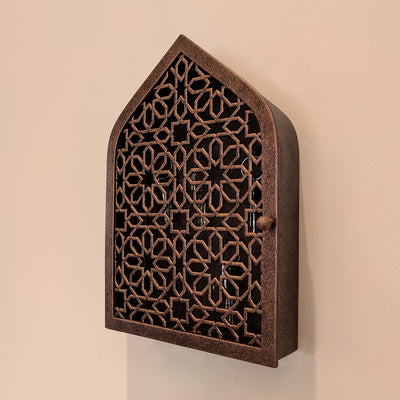 A wall mounted closed key cabinet with a geometric pattern and Islamic arched top painted in an antique bronze finish