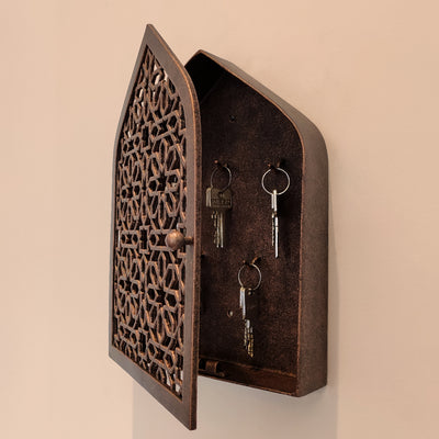 A wall mounted opened key cabinet with a geometric pattern and Islamic arched top painted in an antique bronze finish