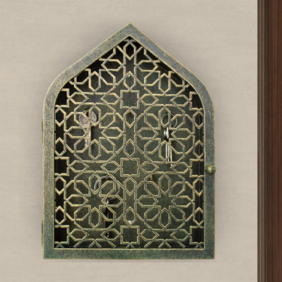 A wall mounted closed key cabinet with a geometric pattern and Islamic arched top painted in an antique green-gold finish