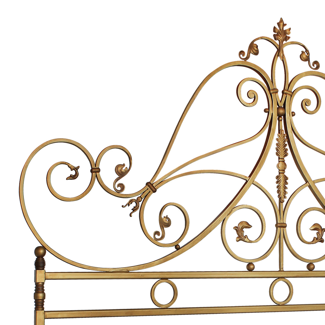 Close up of a wrought iron headboard made up of classical scrolls and leaves, painted in an antique golden finish