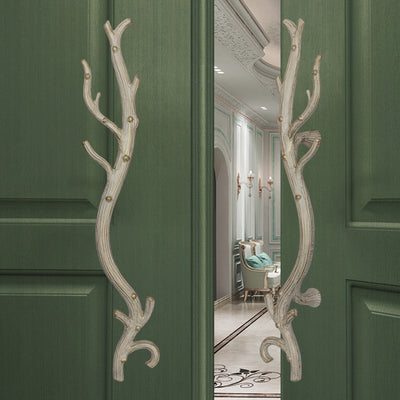 A pair of antique white decorative pull handles inspired by branches mounted on an opened wooden door